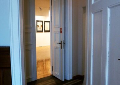 Otwarte drzwi prowadzące do korytarzyka z oryginalna pałacową posadzką. Na wprost drzwi prowadzące z korytarzayka do sali balowej.