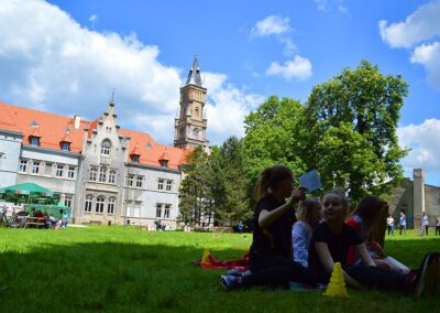Grupka dzieci siedzących na trawniku., w tle pałac w Nakle Śląskim.